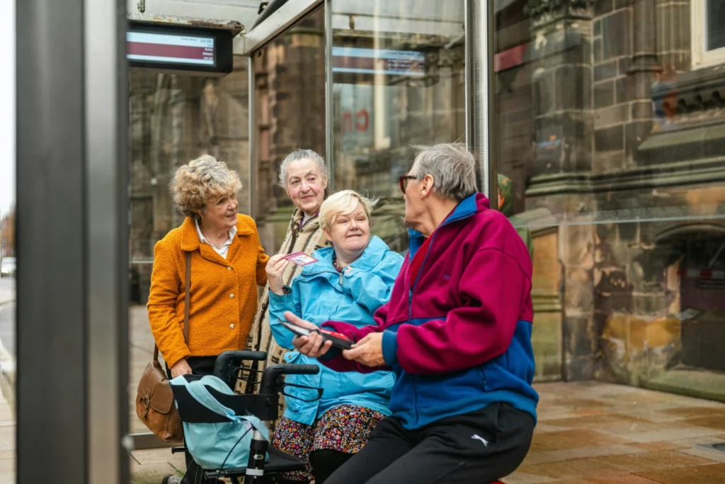 Elderly group at the bus stop with one assisted with a walking aid