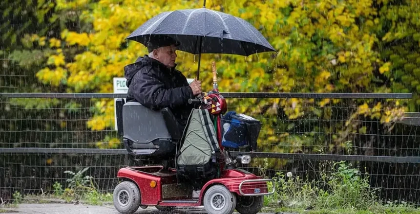 Man riding mobility scooter on pavement on a rainy day with an umbrella