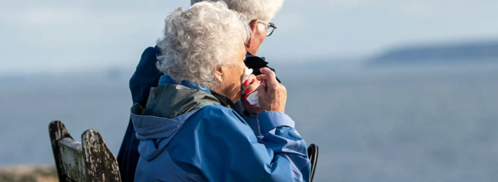 Elderly couple sat on a bench on a hill by the sea